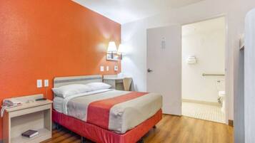 Une chambre d’hôtel comprenant un lit, une table de chevet, une lampe et une porte donnant accès à une salle de bain.
