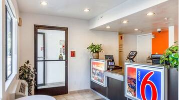 A hotel reception area with a glass door entrance, a reception desk, a digital display, and a sign indicating the hotel number.