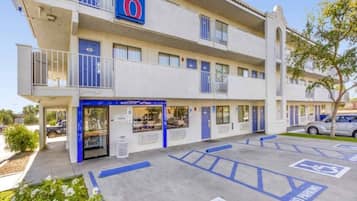 Een motel met meerdere verdiepingen, een blauw bord met het cijfer '6', een gevel en parkeerplaatsen met gehandicapten symbolen.