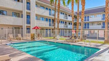 A hotel pool area with a clear blue pool, lounge chairs, and palm trees.