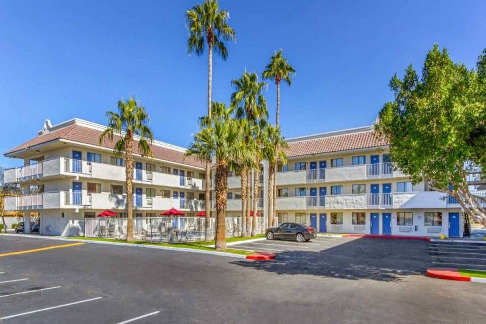 A multi-story hotel with a parking lot, palm trees, and a clear blue sky.