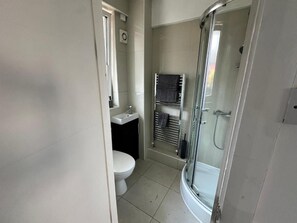 A bathroom with a toilet, sink, towel rack, and a glass-enclosed shower area. - Modern 1-Bed Apartment Southwark (London)