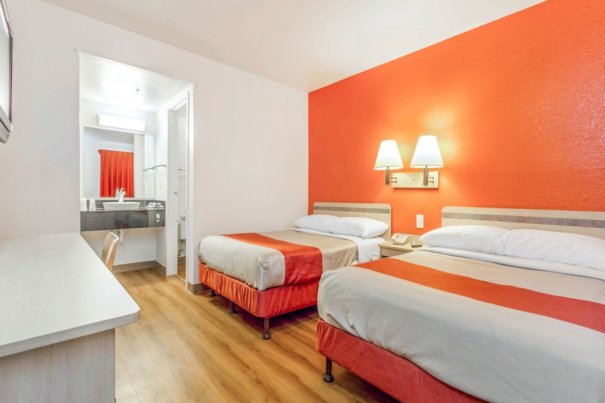 A hotel room with two beds, a desk, and a bathroom.