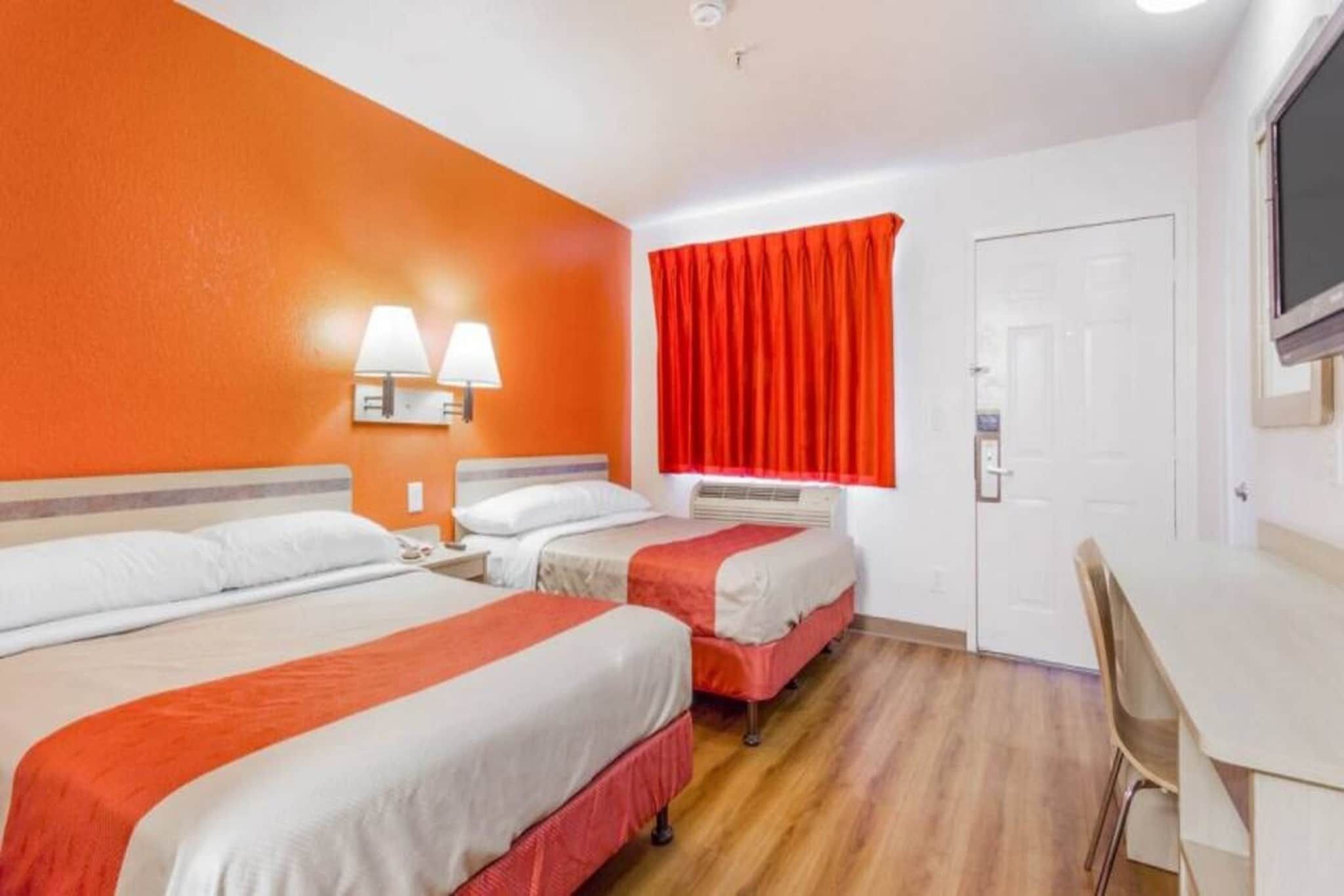 A hotel room with three beds, a desk, and a television.