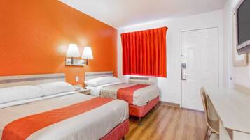 A hotel room with three beds, a desk, and a television.