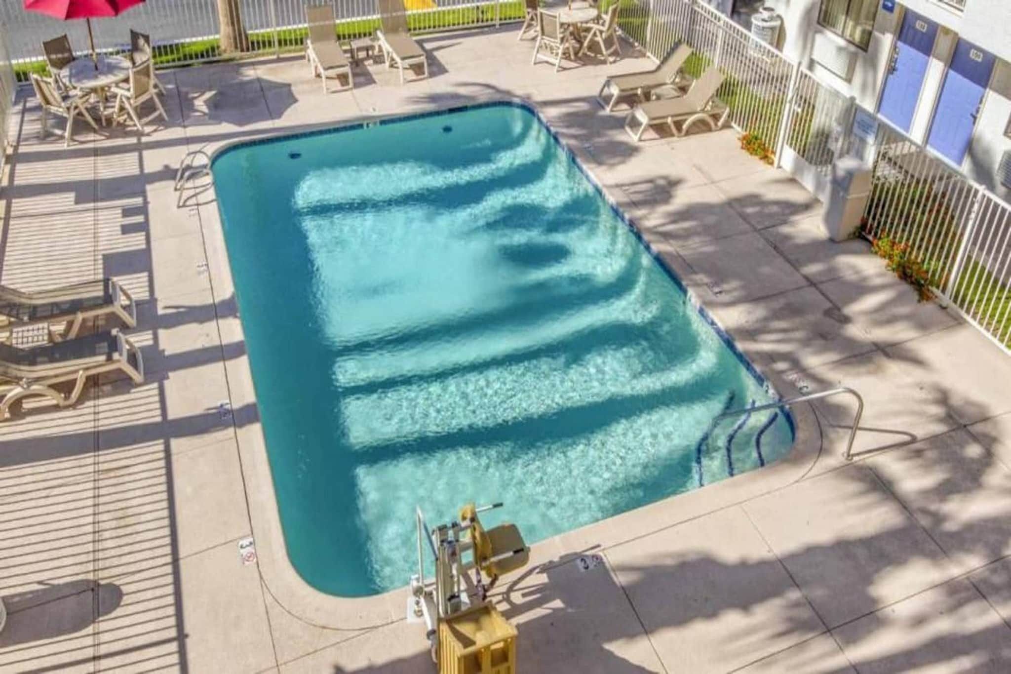 Et rektangulært pool med en soldæk, omgivet af liggestole og et overdækket siddeområde.