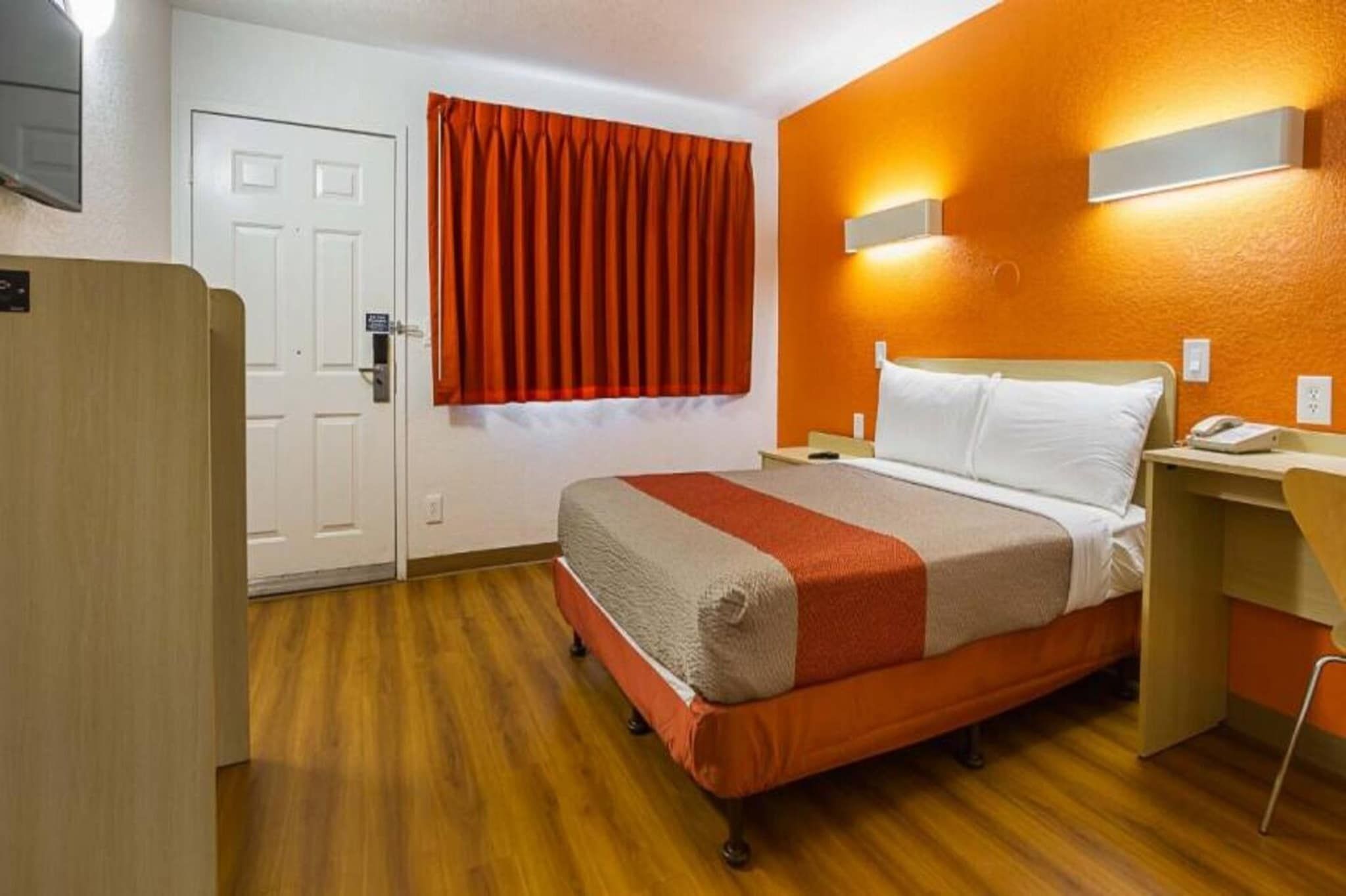 A hotel room with a bed, a desk, a chair, a wardrobe, and a door.