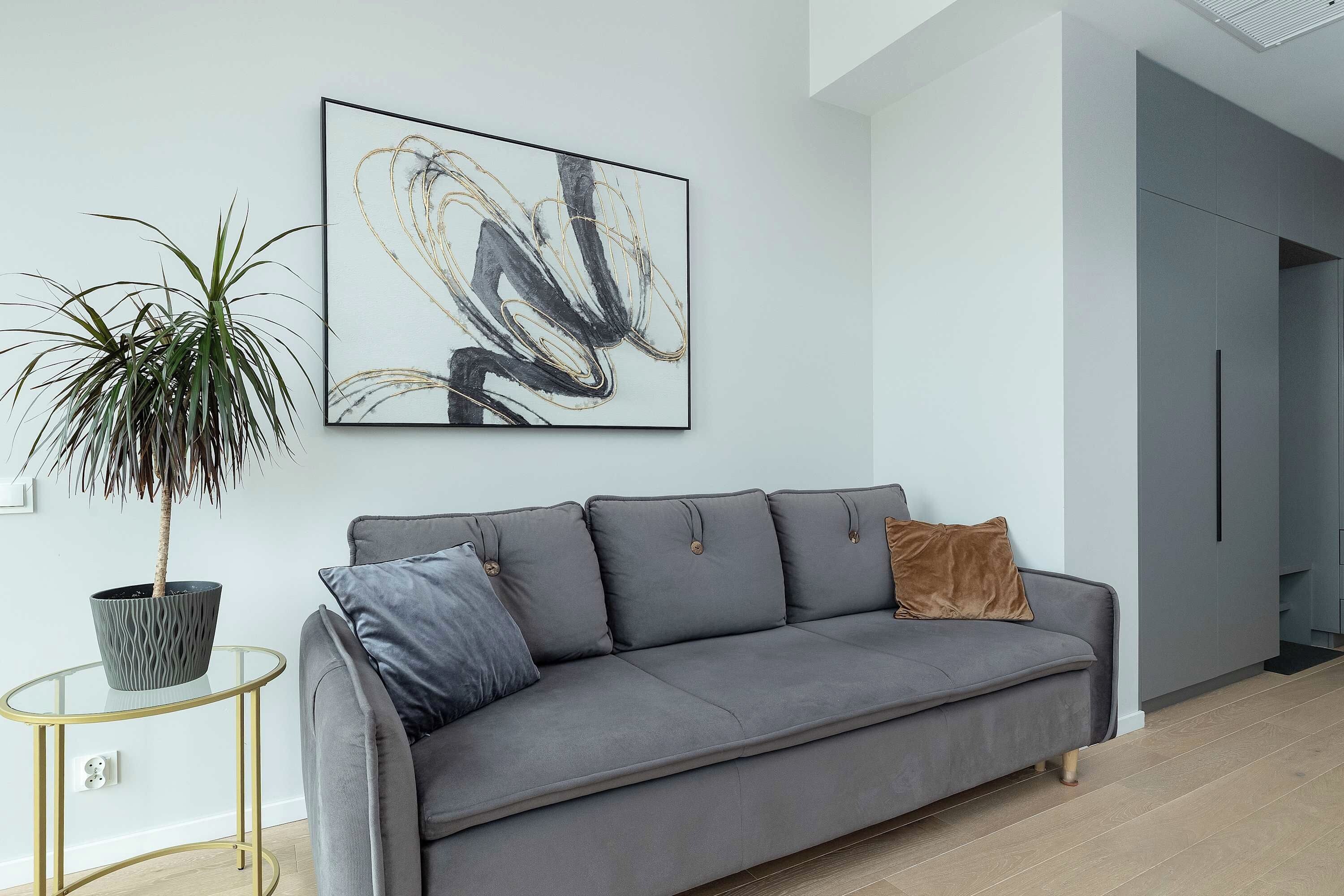Una sala de estar moderna con un sofá gris, una planta en maceta y un cuadro abstracto colgado en la pared.