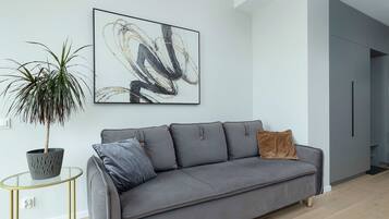 Una sala de estar moderna con un sofá gris, una planta en maceta y un cuadro abstracto colgado en la pared.