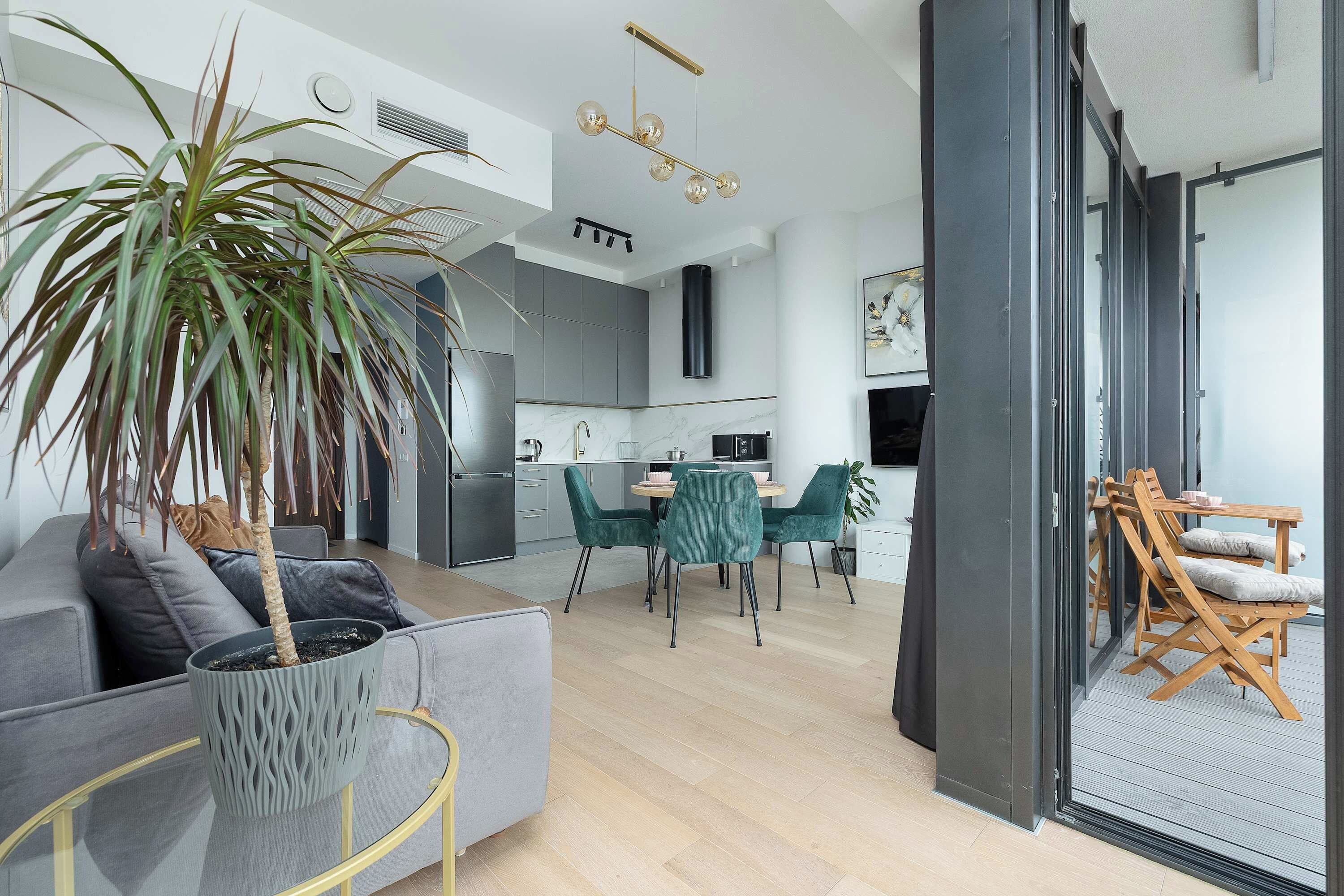 Un espacio habitable moderno con un sofá gris, un área de comedor con sillas verdes, una cocina con armarios grises y un ventanal grande.