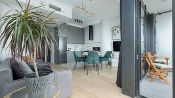 Un espacio habitable moderno con un sofá gris, un área de comedor con sillas verdes, una cocina con armarios grises y un ventanal grande.