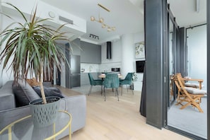 Ein moderner Wohnraum mit grauem Sofa, einem Essbereich mit grünen Stühlen, einer Küche mit grauen Schränken und einem großen Fenster.