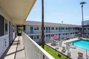A motel with a pool area, including a fenced deck with chairs and umbrellas. - 1 Queen Bed | Mini Fridge (MESA)