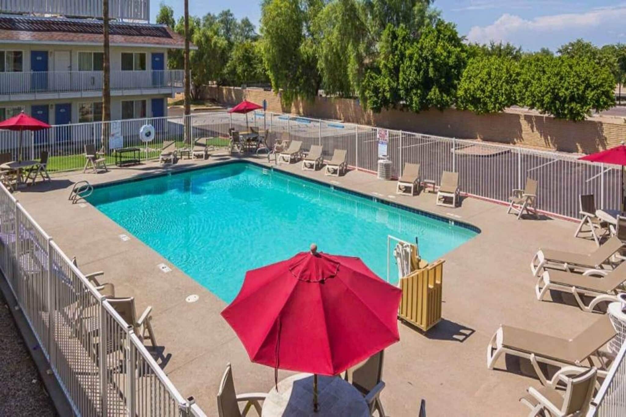 A rectangular swimming pool with a red umbrella, surrounded by lounge chairs and a fence.