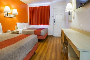 Ein Hotelzimmer mit zwei Betten, einem Schreibtisch, einem Sessel, einem Fernseher und einer Tür.