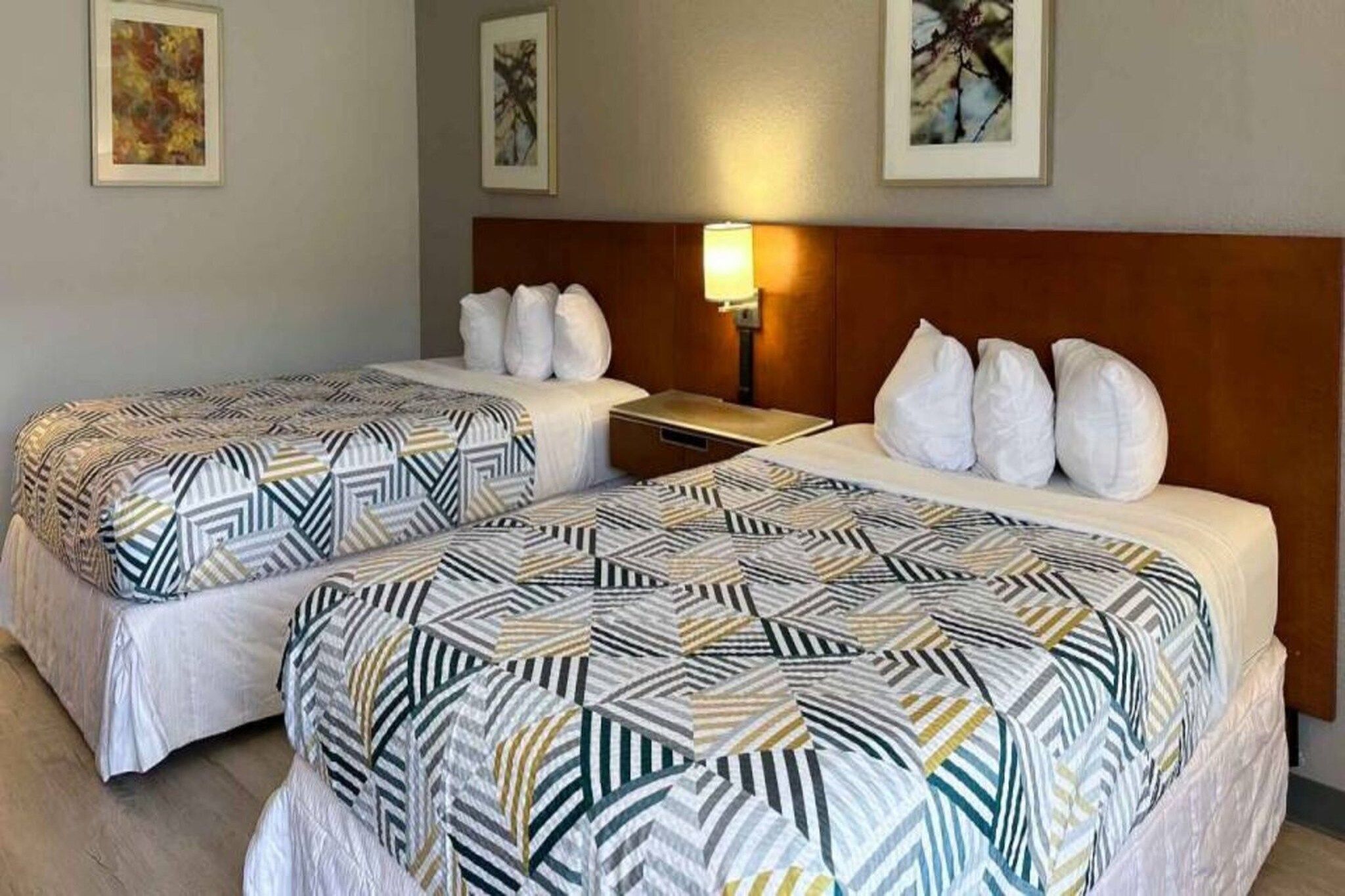 A hotel room with two beds, each with patterned bedding, a nightstand, a lamp, and framed artwork on the walls.