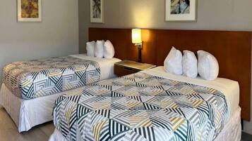 A hotel room with two beds, each with patterned bedding, a nightstand, a lamp, and framed artwork on the walls.
