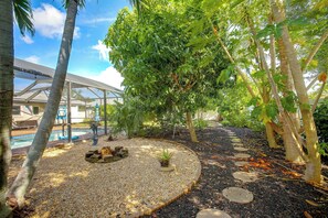 Un jardín con piscina, palmeras y una zona exterior cubierta.