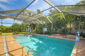 Ein Schwimmbecken mit Überdachung, umgeben von Bäumen und blauem Himmel.
