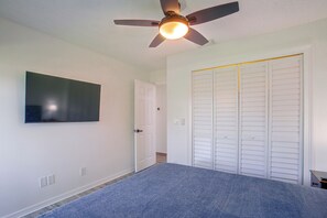 Ein Schlafzimmer mit Deckenventilator, Flachbildfernseher an der Wand, geschlossener Tür und Schrank mit Schiebetüren.