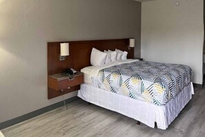 A hotel room with a bed, a nightstand, a telephone, and a wall-mounted lamp.