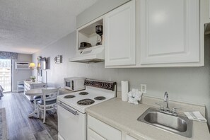 A compact kitchen with white cabinets, a stove, a microwave, and a sink. - Beachfront Bliss & Ocean Views: Myrtle Beach Gem (Myrtle Beach)