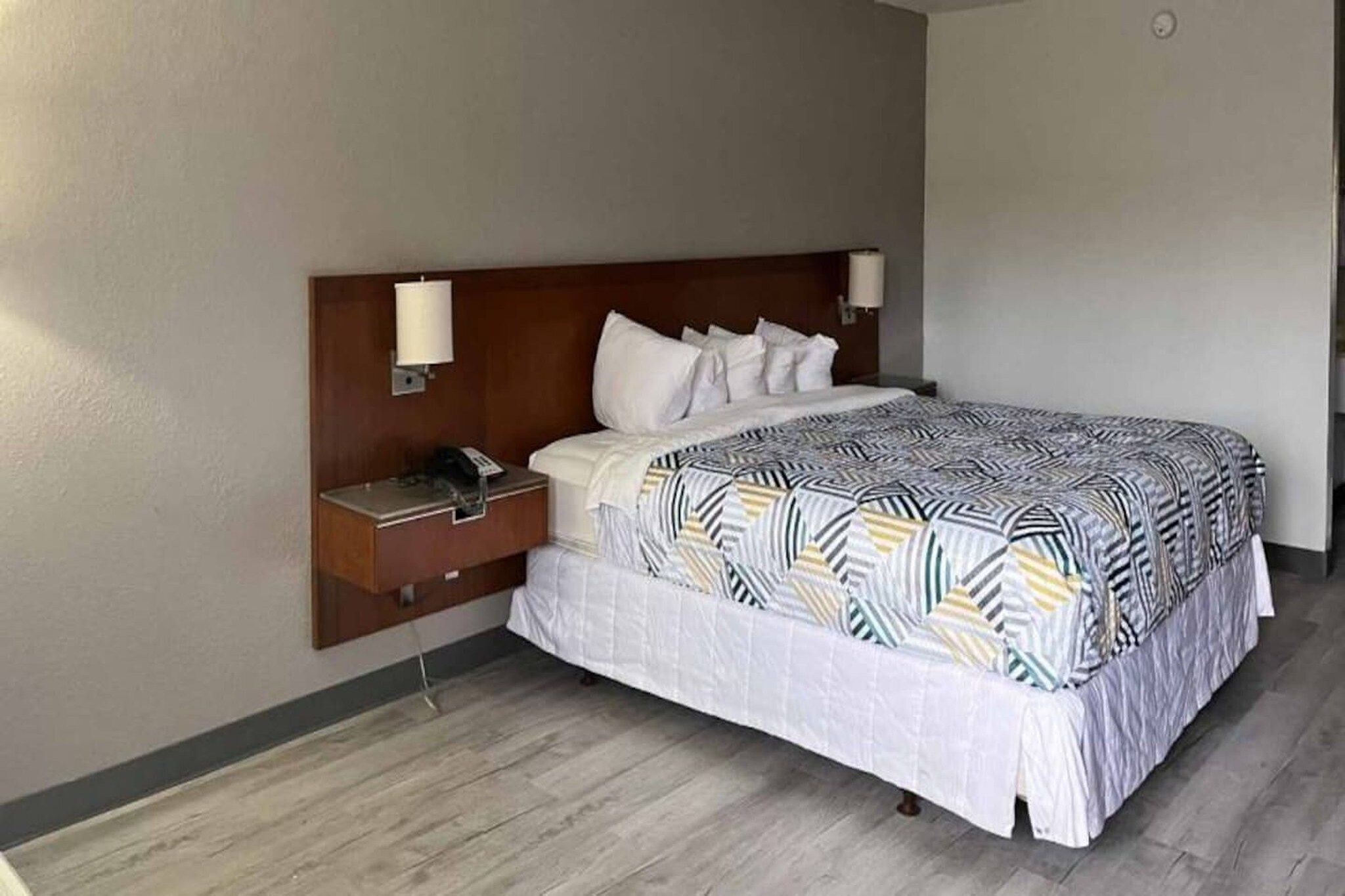 A hotel room with a bed, a nightstand, a lamp, and a wall-mounted phone.