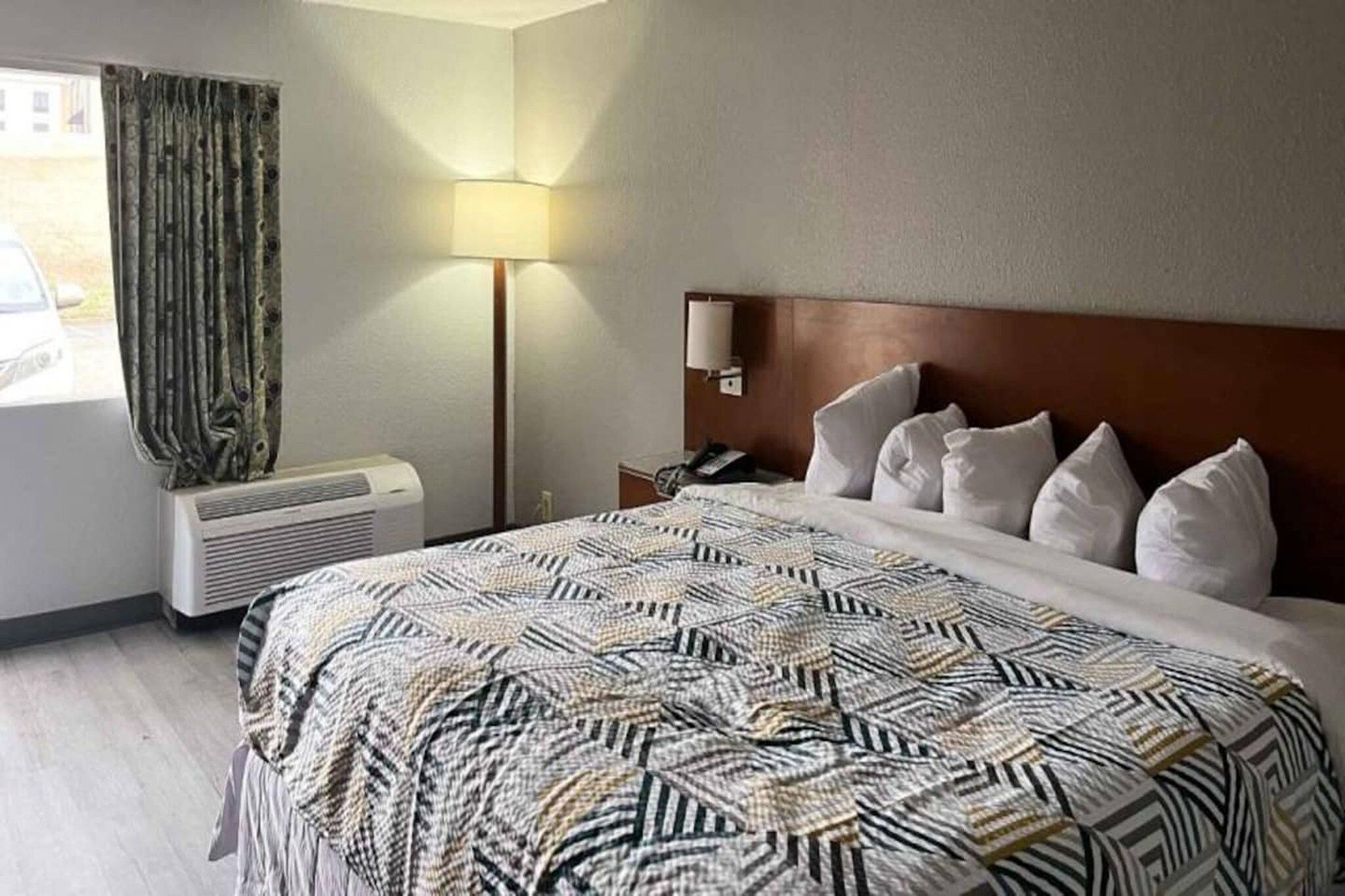 Habitación de hotel con cama, lámpara de noche, teléfono y ventana con cortinas.