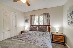 Een slaapkamer met een bed, twee nachtkastjes, een plafondventilator, een raam met gordijnen en een aan de muur hangend schilderij.