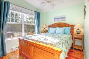 Ein Schlafzimmer mit einem hölzernen Bett, zwei Nachttischlampen, einem Fenster mit Vorhängen und einem Deckenventilator.