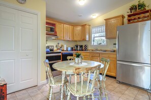 A kitchen with wooden cabinets, a stainless steel refrigerator, a dining table with chairs, and a window with a view. - Charming Coastal Getaway in Wells, Maine (Wells)