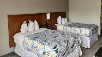 Two double beds with patterned bedding, a wooden headboard, a bedside table with a lamp, and a white pillow.