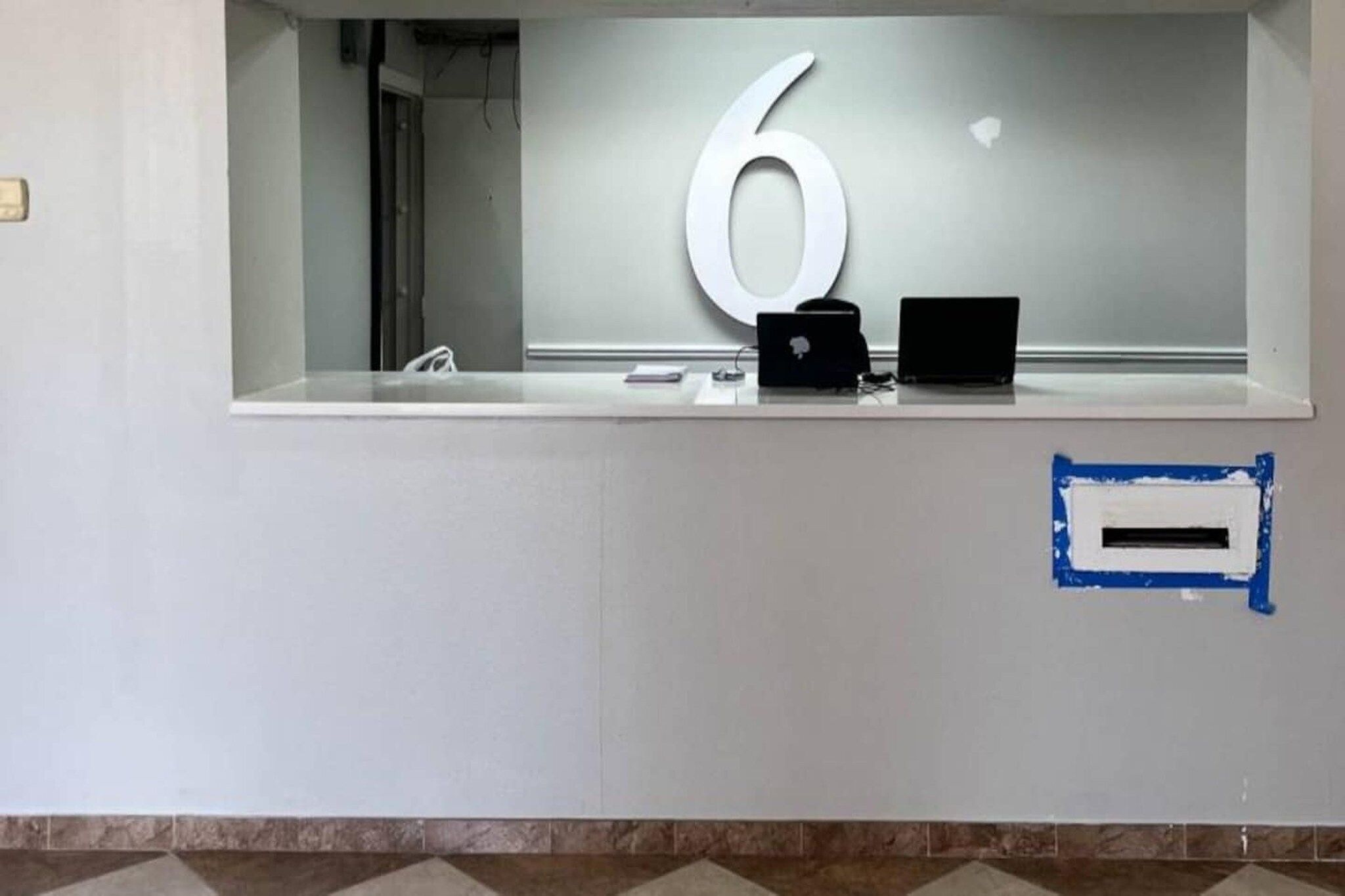 Un mostrador de recepción con un letrero grande con el número 6, una laptop y un dispositivo pequeño en la barra.