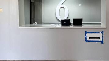 Un mostrador de recepción con un letrero grande con el número 6, una laptop y un dispositivo pequeño en la barra.