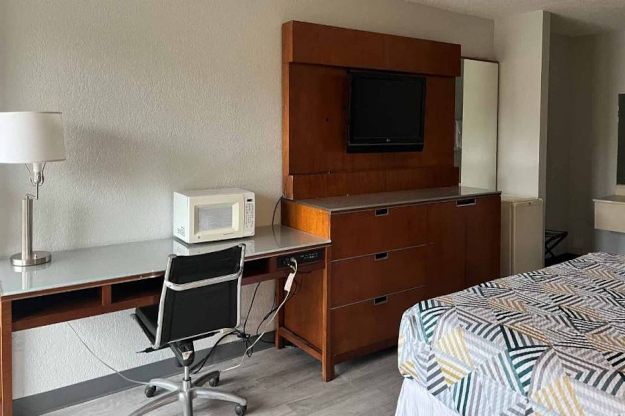 Quarto de hotel com escrivaninha, cadeira, cama, televisão e micro-ondas.