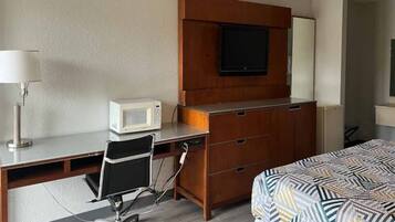 Quarto de hotel com escrivaninha, cadeira, cama, televisão e micro-ondas.