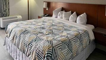 Una habitación de hotel con una cama grande, una mesita de noche, una lámpara y un aire acondicionado.