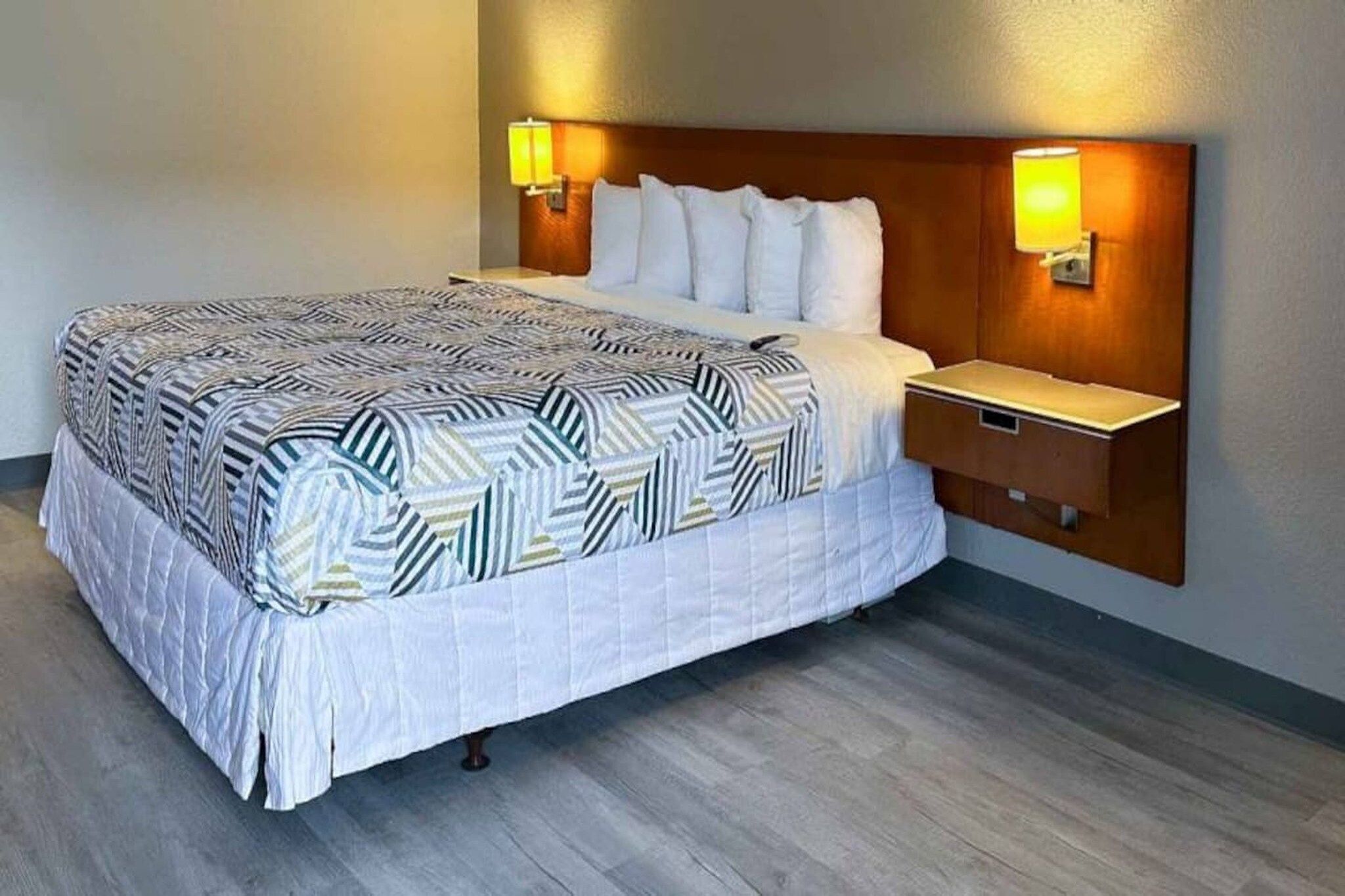 Una habitación de hotel con una cama grande, un cabecero de madera, dos lámparas de noche y una mesita de noche.