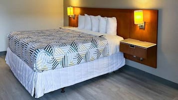 Una habitación de hotel con una cama grande, un cabecero de madera, dos lámparas de noche y una mesita de noche.