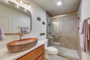Un baño con lavamanos de madera, inodoro, ducha con mampara de vidrio y espejo con iluminación.