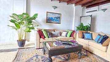 A living room with a wooden ceiling, a chandelier, a sofa set, a coffee table, and a large potted plant.
