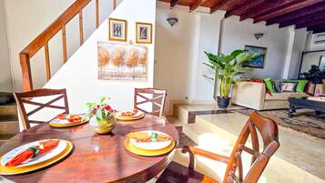 A dining area with a wooden table, chairs, and a staircase leading to a living room with a couch and a plant.