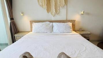 A hotel room with a large bed, two bedside tables, a wall-mounted light fixture, and a window with curtains.