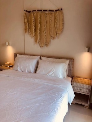 Uma cama com roupa de cama branca, duas mesas de cabeceira com abajures e um quadro pendurado acima da cama.