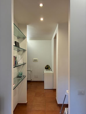 Ein enger Flur mit einer Glastrennwand links, einem weißen Heizkörper und einem kleinen, weißen Schrank mit Blumen rechts.