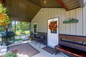 A covered porch with a grill, seating, and a welcome mat.