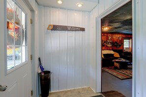 A hallway with a 'Welcome' sign, a trash can, and a glimpse into a room with a patterned rug and a couch.