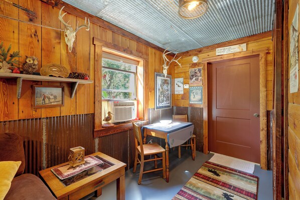 A rustic interior with wooden walls, a dining table, chairs, a bench, and a fireplace.