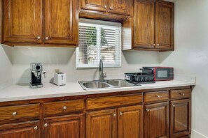 A kitchen with wooden cabinets, a stainless steel sink, a coffee maker, a toaster, and a microwave. - Fullerton Suite w/ Private Yard, Extended Stays (Fullerton)