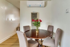 A conference room with a round table, four chairs, a vase with red flowers, an air conditioning unit, and a window with blinds. - Fullerton Suite w/ Private Yard, Extended Stays (Fullerton)